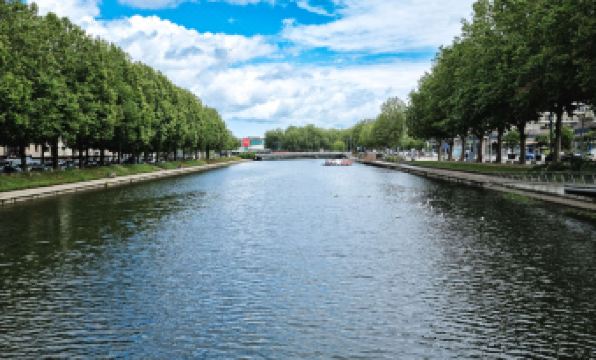 a serene river with trees lining both sides , and people walking on the other side of the river at Ibis Styles Caen Centre Gare