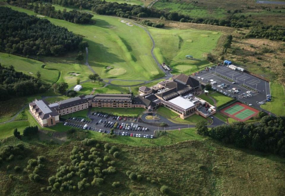 aerial view of a large hotel surrounded by green grass and trees , with cars parked in the parking lot at DoubleTree by Hilton Glasgow Westerwood Spa & Golf Resort