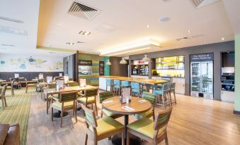 a modern cafe with wooden tables and chairs , a bar area , and shelves stocked with bottles at Premier Inn Melton Mowbray