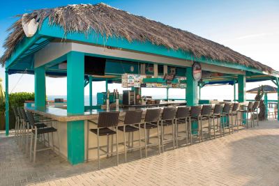 a beach bar with a thatched roof , surrounded by clear blue water and lush greenery at Wyndham Reef Resort Grand Cayman