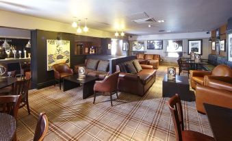 a cozy living room with brown leather couches , chairs , and a coffee table , decorated with various posters and posters on the walls at Village Hotel Chester St David's