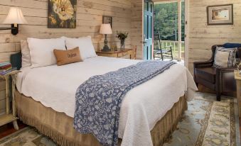 a cozy bedroom with a large bed , white bedding , and blue comforter , situated next to a window that overlooks a balcony at Glen-Ella Springs Inn