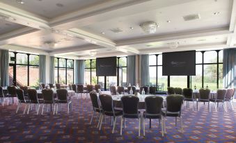 a large conference room with rows of chairs and tables , all facing windows , and two screens on the walls at Rookery Hall Hotel & Spa