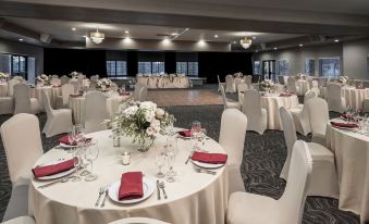 a well - decorated banquet hall with multiple tables set up for a formal event , including white tablecloths and red napkins at London Bridge Resort