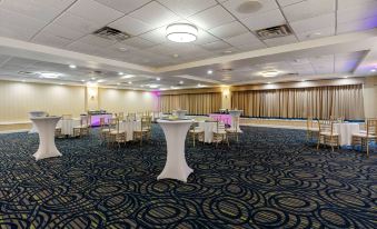 a large , empty banquet hall with white tables and chairs , blue carpet , and a chandelier hanging from the ceiling at Wyndham Garden Manassas
