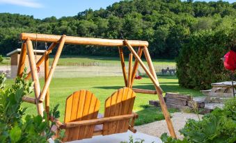 a wooden swing hanging from a tree in a grassy field , with a chair and trees in the background at Justin Trails Resort
