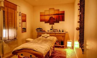 a massage table in a dimly lit room , surrounded by various items such as chairs , books , and a cell phone at La Bastide