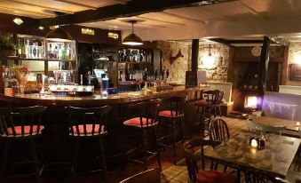 a cozy bar with wooden chairs , tables , and a variety of bottles on the counter at Queens Head Inn