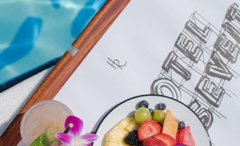 a plate of fruit salad with a cup of juice and a vase with flowers on the side at The Hollywood Roosevelt