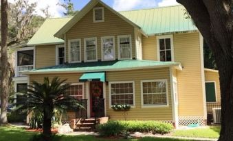 a yellow and green house with a porch and palm trees in front of it at Dolan House B&B