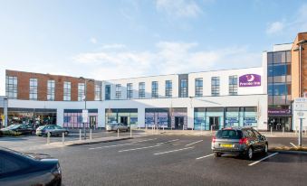 a large parking lot with several cars , including a white car and a purple car , parked in front of a building with multiple windows at Premier Inn Trowbridge