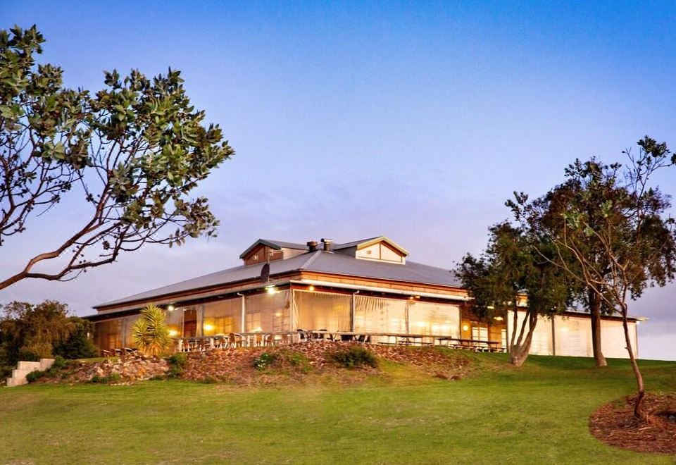 a large building surrounded by a grassy field , with a tree in the foreground and a fence surrounding the area at Bremer Bay Resort