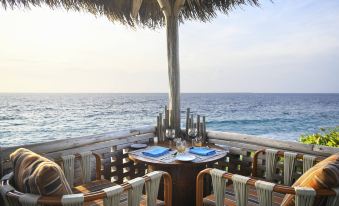 an outdoor dining area with a table set for two people , surrounded by chairs and a gazebo overlooking the ocean at JW Marriott Maldives Resort & Spa