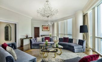 a modern living room with a large window , blue sofas , and a chandelier , along with other furniture at The Ritz-Carlton, Doha