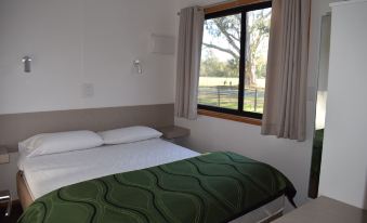 a bed with a green blanket is situated next to a window in a room at Cohuna Waterfront Holiday Park
