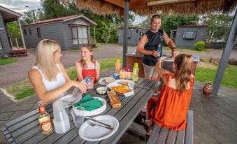 a family is enjoying a meal together at an outdoor picnic table , surrounded by food and drinks at Adelaide Caravan Park - Aspen Holiday Parks