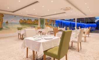 a restaurant with white tables and chairs , a large painting on the wall , and blue lighting at Lagoa Hotel