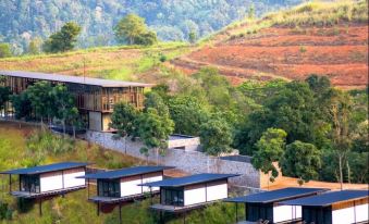 a row of wooden houses on a hillside , surrounded by lush greenery and a beautiful landscape at Santani Wellness Kandy