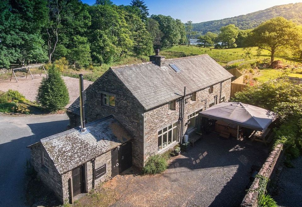 an aerial view of a large stone house surrounded by trees and grass , with a pond in the background at Lakeside Cottage