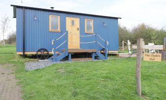 a blue and yellow cabin with a wooden deck and stairs , situated on a grassy field at The Clydes