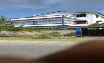 a large , white building with blue accents is situated on a dirt road in front of trees at Blue Rooms