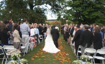 a wedding ceremony taking place outdoors , with the bride and groom being walked down the aisle by their parents at Inn at Mitchell House