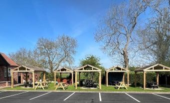 a parking lot with several wooden picnic tables and benches , surrounded by trees and a clear blue sky at The Black Horse Inn