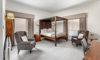 a large bedroom with a canopy bed , two armchairs , and a rug on the floor at Reigate Manor Hotel