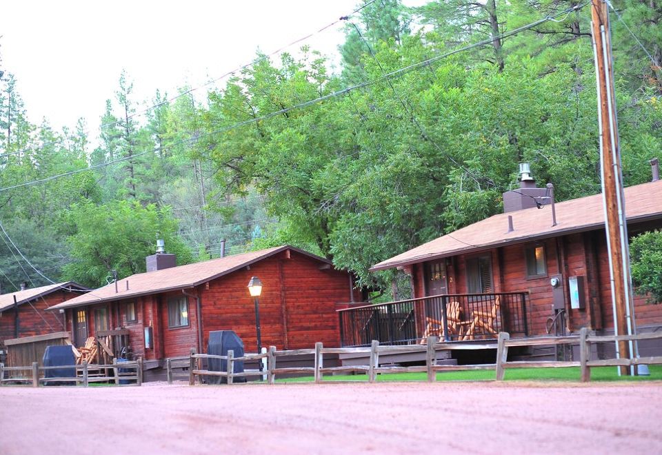 two red wooden cabins are sitting next to each other in a wooded area , surrounded by trees at Kohl's Ranch Lodge
