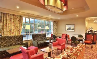 a large , well - lit hotel lobby with various seating options , including couches and chairs , as well as a television at Reigate Manor Hotel
