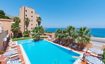 a large swimming pool surrounded by lounge chairs and palm trees , with a building in the background at Hotel Punta Nord Est