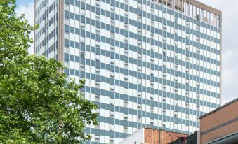a tall building with a red and white sign on the top has a tree in front at Hampton by Hilton Birmingham Broad Street