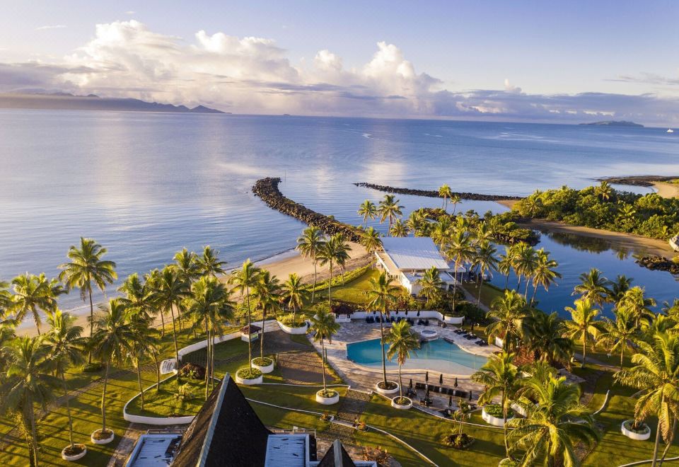 an aerial view of a resort with palm trees , a pool , and a body of water at The Pearl South Pacific Resort