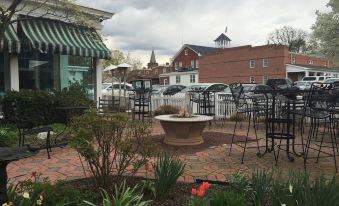 a brick patio with a fire pit and several chairs , surrounded by potted plants and buildings in the background at The Brick Hotel