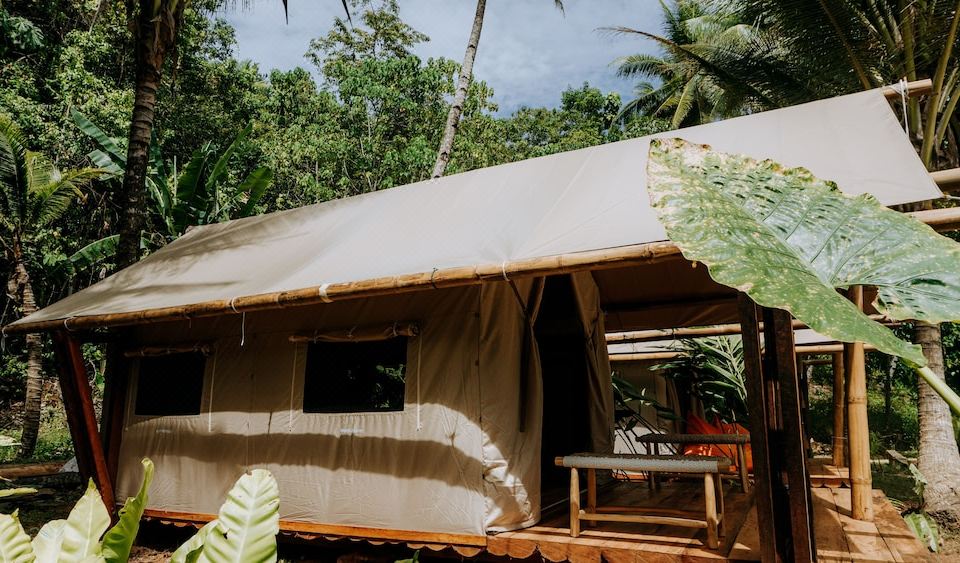 a small wooden house with a large beige canopy is nestled in a tropical setting at Moro Ma Doto