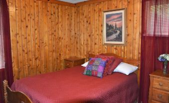 a cozy bedroom with wooden walls , a red bed , and a painting on the wall at Lost Lodge Resort