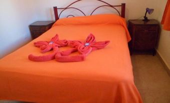a bedroom with an orange bedspread and two pink slippers on it , creating a cozy atmosphere at Alquimia