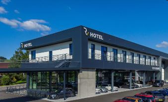 a modern hotel building with a large parking lot and several cars parked outside , under a clear blue sky at Self Check-in Hotel Von Rotz