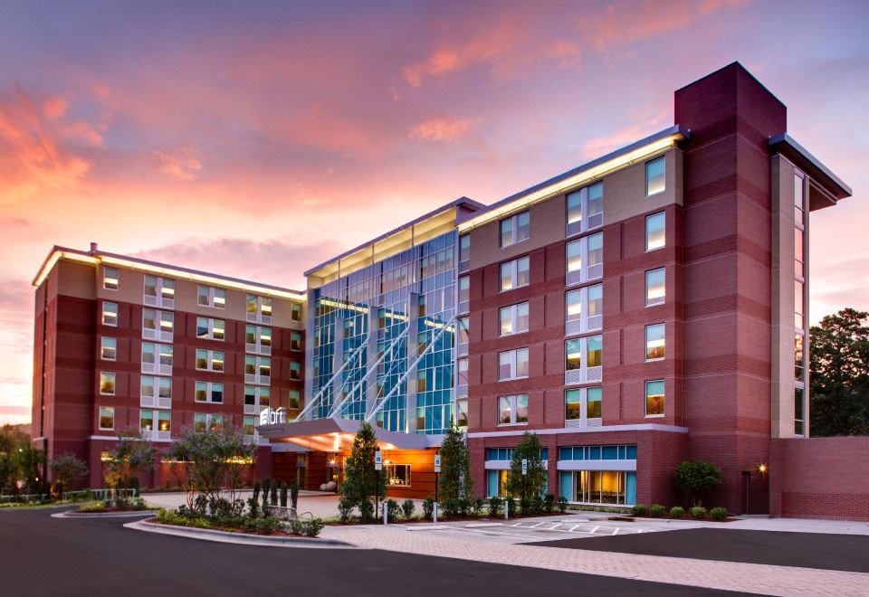 a large , modern hotel building with multiple levels and windows , surrounded by trees and a parking lot at Aloft Chapel Hill