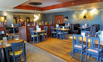 a restaurant with wooden floors and blue chairs , tables , and a bar in the background at York North West