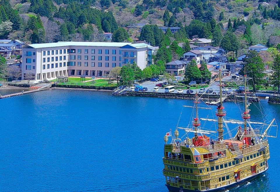 a large yellow boat floating on a body of water near a building , surrounded by trees and mountains at Hakone Hotel