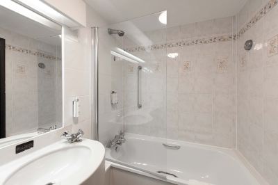 a bathroom with white tiled walls , a bathtub with a glass door , and a shower area at Village Hotel Liverpool