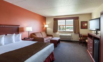 a hotel room with a bed , couch , and dining table , all set against a coral - colored wall at AmericInn by Wyndham Valley City Conference Center