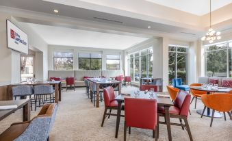 a large dining room with multiple tables and chairs , some of which are red in color at Hilton Garden Inn Gilroy