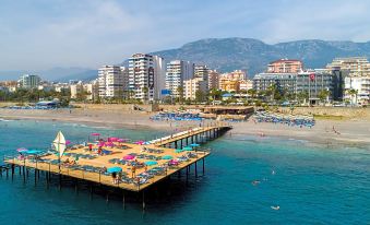 a beach scene with a pier extending into the ocean , surrounded by a crowd of people enjoying their time on the beach at Senza Grand Santana Hotel