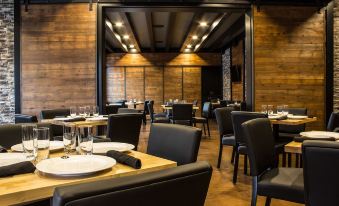 a restaurant with wooden walls , black tables and chairs , and a dining area filled with white plates and wine glasses at Cobblestone Hotel & Suites - Chippewa Falls