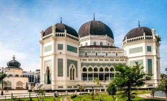 a grand , white building with black domes and white columns , surrounded by lush green trees and clear skies at Alpha Inn