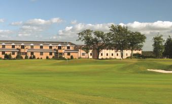 a large building with a red roof is in the background of a green golf course at DoubleTree by Hilton Glasgow Westerwood Spa & Golf Resort
