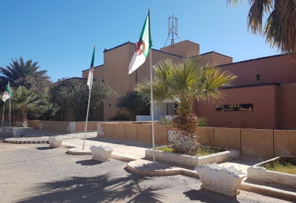 a large building with two flags on poles in front of it , surrounded by trees at Antar hotel