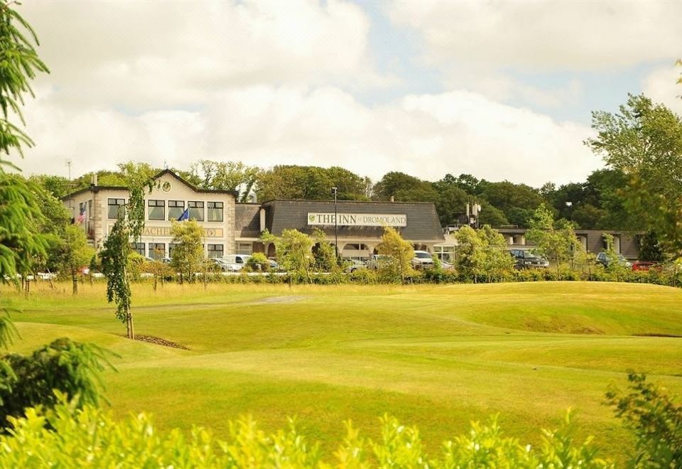 a large building with a blue sign is surrounded by trees and grass , with a golf course in the foreground at The Inn at Dromoland